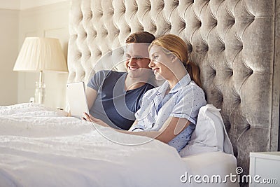 Couple At Home In Bed Self Isolating Using Digital Tablet During Covid 19 Lockdown Stock Photo