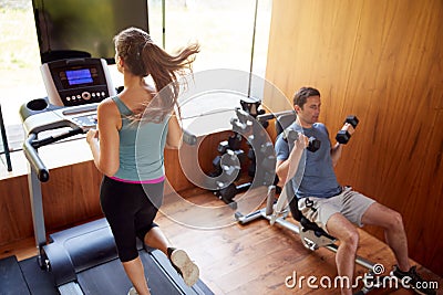 Couple In Home Gym Exercising With Weights And Using Running Machine Stock Photo