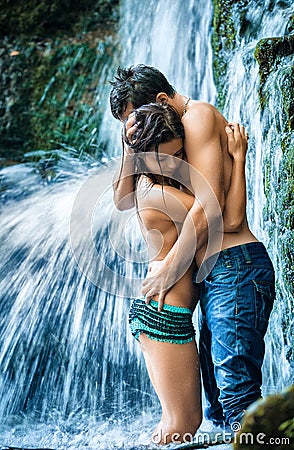 Couple hugging and kissing under waterfall Stock Photo