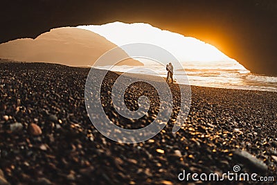 Couple kissing under arch on Legzira ocean beach and enjoying fantastic sunset Stock Photo