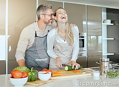 Couple in kitchen cooking together in their home, having fun and laughing. Middle aged man and woman cutting healthy Stock Photo