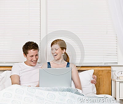 Couple laughing and using laptop in bed Stock Photo