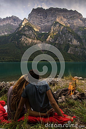 Couple looking at each other and relaxing in the front of a beautiful lake from Switzerland with fire beside. Stock Photo