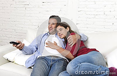Couple in love cuddling on home couch relaxing watching movie on television with man holding remote control Stock Photo