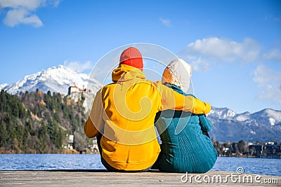 Couple in love hugging together with colorful cloths sitting and relaxing on a wooden pier on a clear sky sunny winter day view fr Stock Photo