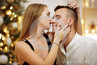 Couple in love kisses and hugs on the sofa near the Christmas tree lights. New year`s night. Christmas Stock Photo