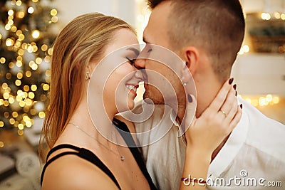 Couple in love kisses and hugs on the sofa near the Christmas tree lights. New year`s night. Christmas Stock Photo