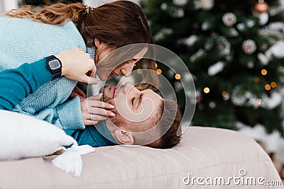 Couple in love lie on bed and want to kiss. garlands on the wall and Christmas tree near the bed Stock Photo