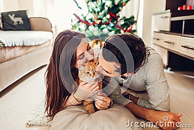 Couple in love lying by Christmas tree and playing with cat at home. Man and woman relaxing Stock Photo