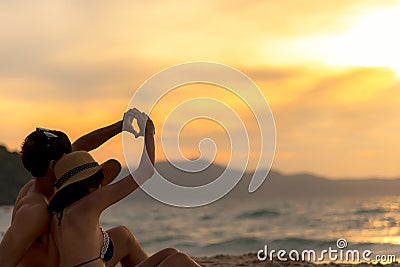 Couple in love making a heart - shape with hands on tropical on the sunset beach in holiday. Stock Photo