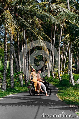 A couple in love on a scooter among the palm trees. Happy couple on vacation in Bali. The couple travels the world. Vacation in Stock Photo