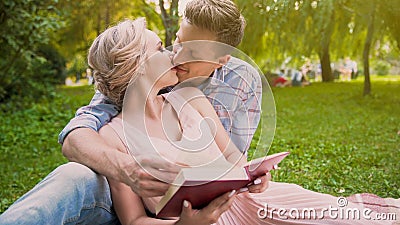 Couple in love sitting on rug reading book together, gently kissing in breaks Stock Photo