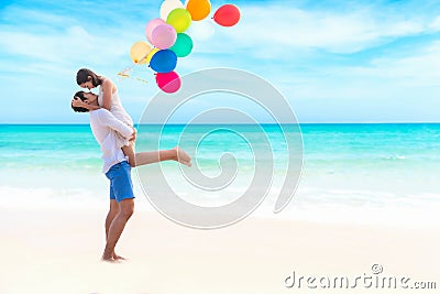 Couple in love. Smiling asian young man is holding girlfriend in his arms on the beach with multi color balloon, Stock Photo