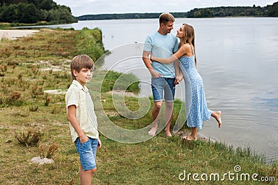 A couple in love are standing on the beach, on the banks of a river. Their son is standing next to them Stock Photo