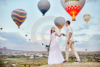 Couple in love stands on background of balloons in Cappadocia. Man and a woman on hill look at a large number of flying balloons Stock Photo