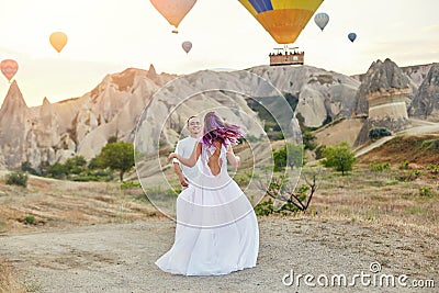 Couple in love stands on background of balloons in Cappadocia. Man and a woman on hill look at a large number of flying balloons Stock Photo