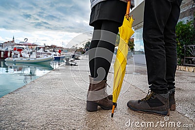 Couple in love stopped while walking along the embankment of resort town after the rain, view of small yacht dock, legs Stock Photo