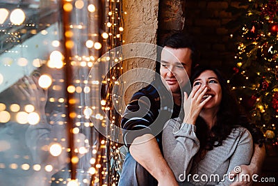 Couple of lovers hugs sitting on the windowsill in the Christmas loft studio. guy is hugging the girl. Stock Photo