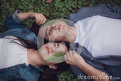 Couple lying in the woods next to each other with a leaf on their face Stock Photo