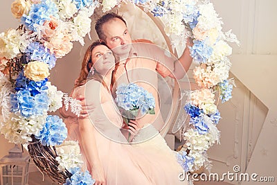 Couple man and woman on a swing in flowers. Studio portrait of an adult couple in pink clothes Stock Photo