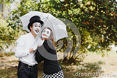 A couple of mimes walk along the pavement under umbrellas. Enamored mimes jump Stock Photo