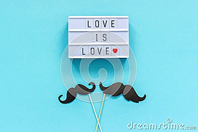 Couple paper mustache props on stick and light box with text Love is love on blue background. Concept Homosexuality gay love. Stock Photo