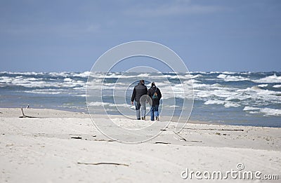 A couple of people strolling on the beach on a rough spring Baltic Sea on a sunny day Editorial Stock Photo