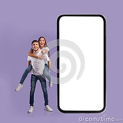 Couple Posing Near Huge Cellphone Screen Pointing Finger, Purple Background Stock Photo