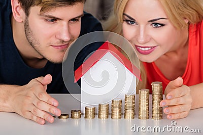 Couple Protecting House Model With Stacked Coins Stock Photo