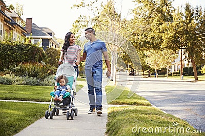 Couple Push Daughter In Stroller As They Walk Along Street Stock Photo