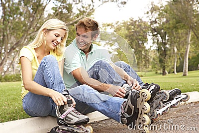 Couple Putting On In Line Skates In Park Stock Photo