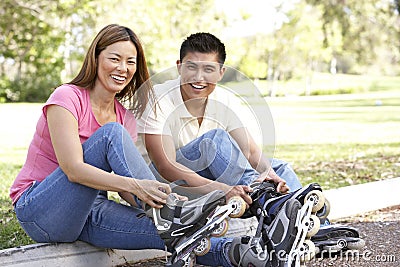 Couple Putting On In Line Skates In Park Stock Photo