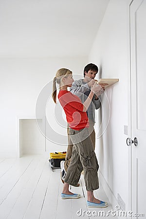 Couple Putting Up Shelf In New Home Stock Photo