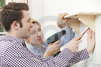 Couple Putting Up Wooden Shelf Together At Home Stock Photo