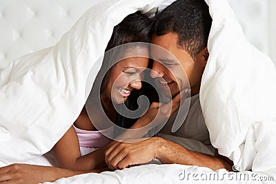 Couple Relaxing In Bed Hiding Under Duvet Stock Photo