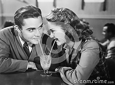 Couple in a restaurant looking at each other and sharing a milk shake with two straws Stock Photo