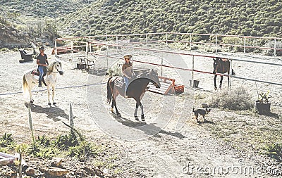 Couple riding horses starting from ranch with their dogs following them - Happy people having fun on summer day - Tour, excursion Stock Photo