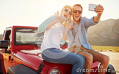 Couple On Road Trip Sit On Convertible Car Taking Selfie Stock Photo