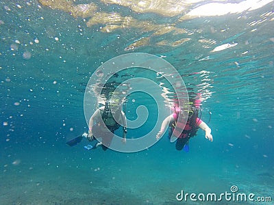 Couple scuba diving under crystal clear water with tank, fins and visor happy swim and share their love doing exercise and living Stock Photo