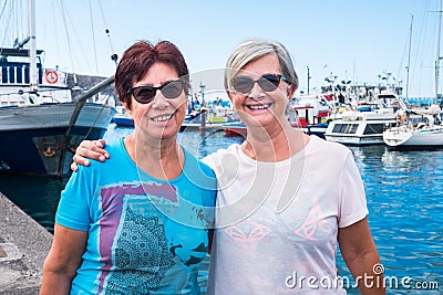 Couple of senior people stay together on pier looking at beautiful port and boats. Smiling senior female friends. Enjoying Stock Photo