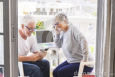 Couple of seniors smiling and looking at the phone with coffe and laptop in the terrace - outoor and outside lifestyle - married Stock Photo