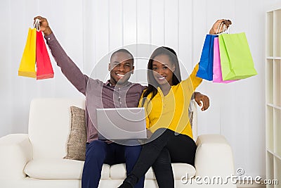 Couple With Shopping Bags And Laptop Sitting On Sofa Stock Photo