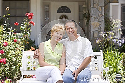 Couple Sitting On Bench Outside House Stock Photo