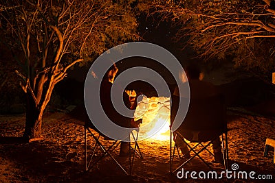 Couple sitting at burning camp fire in the night. Camping in the forest under starry sky, Namibia, Africa. Summer adventures and e Stock Photo