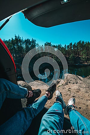 couple sitting in car trunk lake on background. legs in sneakers and jeans Stock Photo