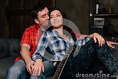 Couple is sitting on the couch with a guitar. Long hair of a brunette with an acoustic guitar. Stock Photo