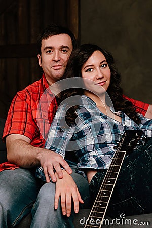 Couple is sitting on the couch with a guitar. Long hair of a brunette with an acoustic guitar. Stock Photo