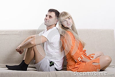 Couple sitting on the couch with his back to each other and looking in the frame Stock Photo