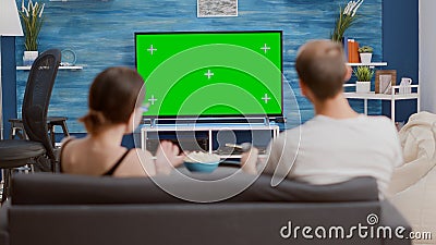 Couple sitting on couch watching television on green screen flat tv talking about favourite show and zapping Stock Photo