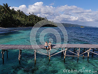 Couple sitting on a dock in a paradise beach in Raja Ampat, Indonesia Stock Photo